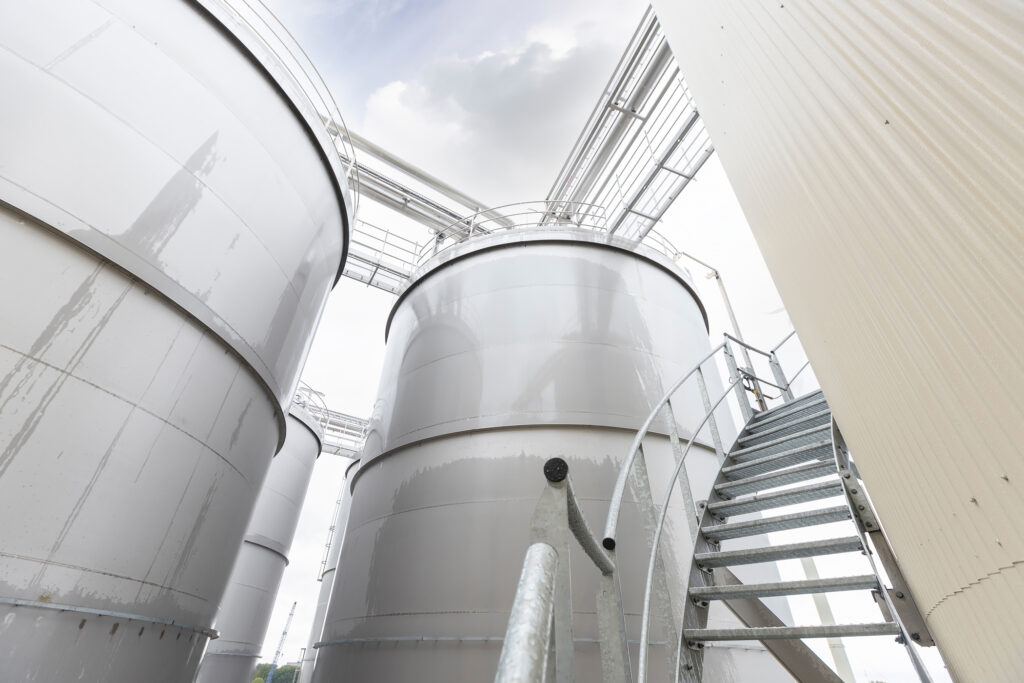 Ein hoher industrieller hygienischen tank mit einem Käfigleiteraufstieg, der seine Größe und Funktionalität in einer Produktionsumgebung unterstreicht.